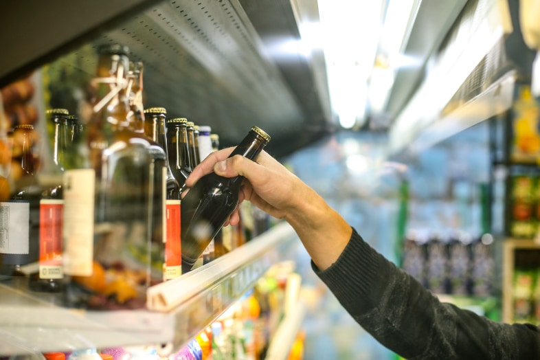Nahaufname eines Bierregals in einem Getränkemarkt, aus dem eine Bierflasche entnommen wird.